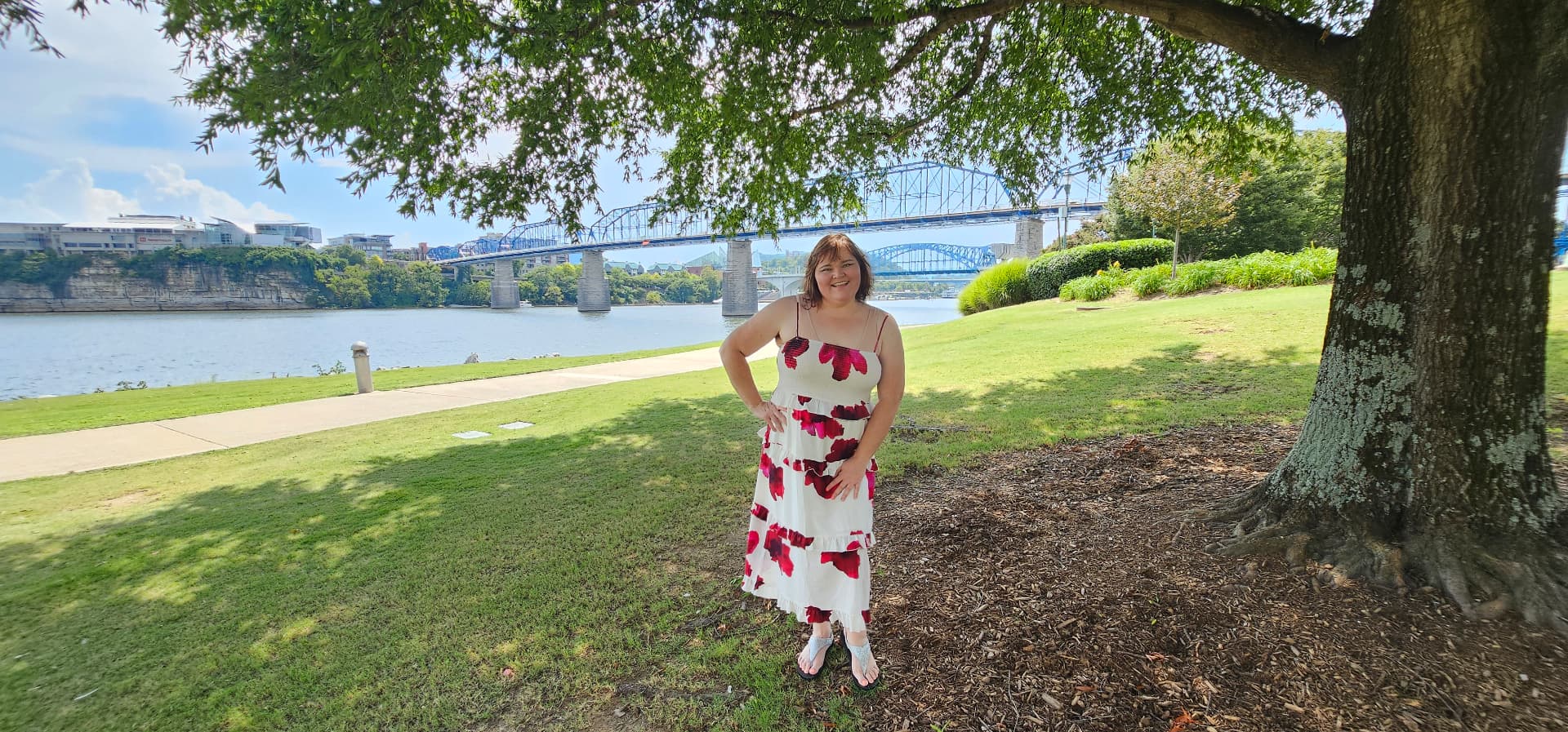 Myra standing under a wide shade tree by the river