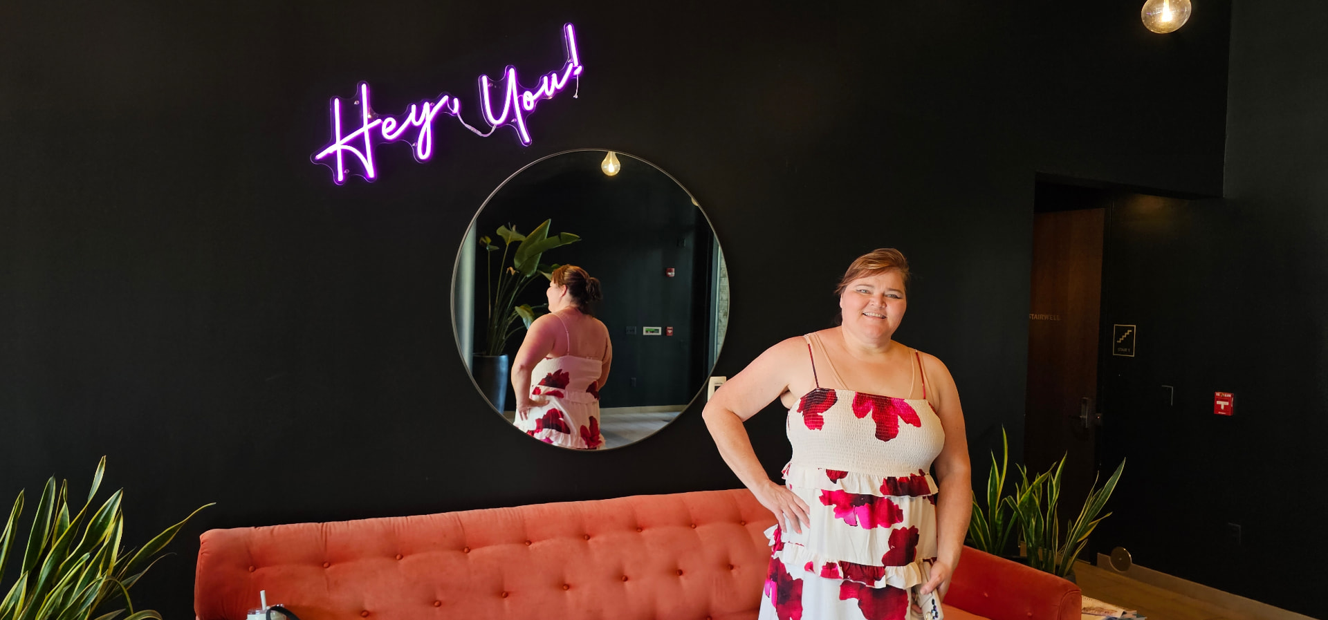 Myra in the lobby with the neon sign and coral sofa